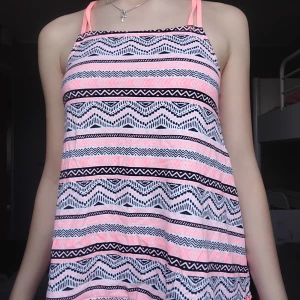 Mönstrad linne-topp från LC Waikiki - Supersöt linne-topp från LC Waikiki med rosa och svarta grafiska mönster på vit botten. Smala axelband som korsas i ryggen och dekorativ bård med små bollar längst ner. Perfekt för varma dagar och ger en chill sommarvibe.