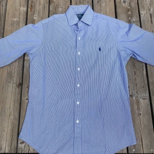 Randig blå skjorta från Polo Ralph Lauren - Snygg blå- och vitrandig skjorta från Polo Ralph Lauren, modell Regent Custom Fit. Nypris: 1600kr