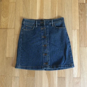Blå jeanskjol från Lee med knappar - A-linjeformad blå jeanskjol från Lee med snygga Lee-knappar framtill, klassiska fickor både fram och bak samt bälteshällor. Passar dig som letar efter en lårlång jeanskjol.💗