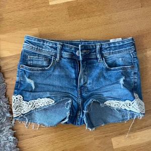 Blå jeansshorts med spetsdetaljer - Snygga blå jeansshorts med råa kanter och slitningar, dekorerade med vita spetsdetaljer. Super snygga💕