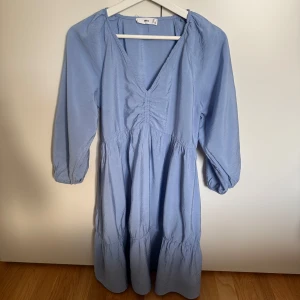 Mango blå klänning, storlek S. Nyskick - •Ljusblå klänning från Mango med v-ringning och trekvartsärmar.  •Använd max. 3 gånger, som ny. Tvättad. •Klänningen har en smickrande passform med rynkdetaljer framtill och en volangkjol. •Modellen har trekvartsärmar med resår och en luftig, flowy passform.  •Perfekt för vår och sommar när du vill känna dig extra fin. •Djurfritt och rökfritt hem.