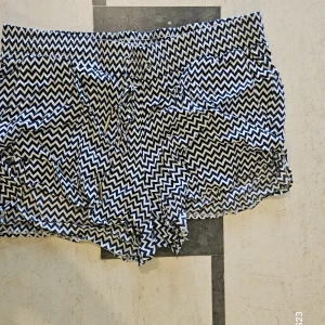 Svartvita mönstrade shorts Gina Tricot - Snygga shorts från Gina Tricot i svartvitt sicksackmönster. De har elastisk midja med snörning och är tillverkade i mjuk bomull. Perfekta för varma dagar när du vill ha en chill och trendig look.