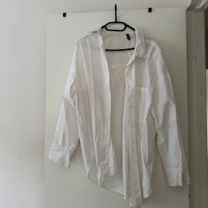 Vit klassisk oversized skjorta från H&M - En vit oversized skjorta från H&M i klassisk modell med lång ärm, krage och knäppning framtill. Skjortan har en bröstficka. Har ett par fläckar från mat som man kan se på bilden. 