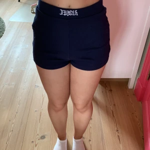 Mörkblå ribbade shorts Angel - Snygga mörkblå ribbade shorts med ett broderat vitt Angel i midjan. De är någorlunda tighta och har hög midja, perfekta för sommarens varma dagar eller som loungewear. Mjukt och stretchigt material som sitter skönt på kroppen.