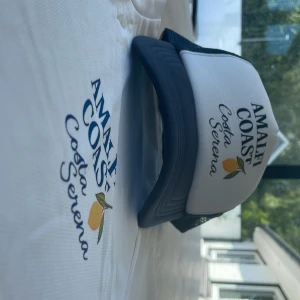 Amalfi Coast truckerkeps blå/vit - Amalfi Coast Special Edition XLJ Beach Club. Keps från Costa Serena ”Amalfi Coast”. Justerbar Storlek. Nytt skick. 