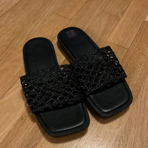 Svarta sandaler med flätad rem - Stilrena svarta sandaler med fyrkantig tå och bred, flätad rem i skinn. Perfekta för sommaren med sin öppna design och trendiga look. Snygga att matcha till både jeans och klänning.
