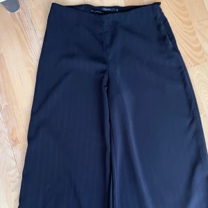 Svarta kostymbyxor - Snygga svarta kostymbyxor med  kritstrecksrandiga detaljer. Vida byxor, och klassisk look, perfekta för en clean och stilren outfit. Materialet känns mjukt och följsamt. 