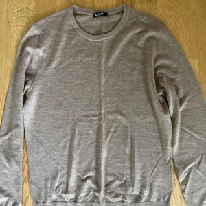Beige stickad tröja Tiger of Sweden - Snygg beige stickad tröja från Tiger of Sweden i klassisk modell. Tröjan har rund halsringning, ribbade muddar och lång ärm. 