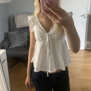 Vit volangblus - Supersöt vit blus med broderade hål, volangärmar och v-ringning med knyt framtill. Aldrig använd 🤍