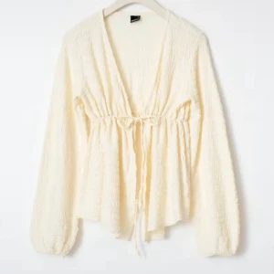 Krämvit blus med knyt och v-ringning - Supersöt krämvit blus med v-ringning och knyt i midjan. Långärmad modell med lätt struktur i tyget och avslappnad passform. Perfekt att styla med jeans eller kjol. Slutsåld hos Gina och är knappast använd 