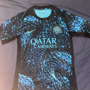 Inter Milan Nike fotbollströja blå/svart - Inter Milan matchtröja från Nike med Qatar Airways som sponsor. Tröjan har ett unikt blått och svart mönster, klubbmärke på bröstet och Nike-logga. Tillverkad i Dri-FIT-material som andas, perfekt för träning eller match. Kortärmad och sportig passform.
