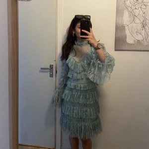 Ljusblå spetsklänning By Malina XS - Superfin ljusblå kortklänning från By Malina i spets med volanger över hela klänningen. Långärmad modell med v-ringning och dragkedja i ryggen. Perfekt för dig som vill sticka ut med romantiska detaljer och unik design.