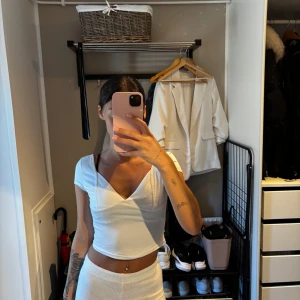 Vit croppad topp från SHEIN - Säljer en vit croppad topp från SHEIN med v-ringning och korta ärmar. Toppen har en snygg omlott-look framtill och öppen rygg. Perfekt för dig som gillar en stilren och fräsch vibe.