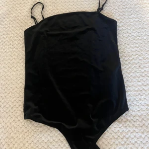 Svart bodysuit - Säljer en svart bodysuit i mjuk sammet med smala axelband och rak skärning upptill. Sitter tight och har en stilren look som passar perfekt till jeans eller kjol. Materialet är glansigt och ger en lyxig känsla. Perfekt för dig som vill ha en enkel men snygg topp. Pris kan diskuteras 