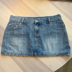 Blå jeanskjol från Stradivarius - Snygg blå jeanskjol från Stradivarius med klassisk femficksdesign, bälteshällor och knappstängning. Kjolen är kort och har coola detaljer som bakfickor med knapp och kontrastsömmar. Perfekt för dig som gillar en avslappnad och trendig stil.