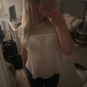 Vit spetsblus med volangärm - Söt vit blus med spets och transparent tyg. Blusen har korta volangärmar och ett fint mönster med lodräta ränder. Knappt använd och i fint skick!