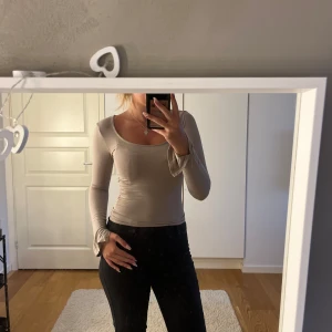 Beige långärmad topp med slits - Snygg beige långärmad topp med rundad, djup urringning och tight passform. Ärmarna har en liten slits vid ärmslutet som ger en extra detalj. Mjuk och stretchig, perfekt att styla med jeans eller kjol. Liten svart fläck på ena armen 