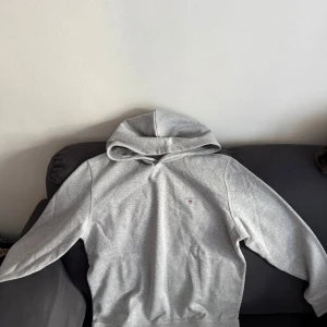 Grå hoodie från Gant - Snygg grå hoodie från Gant med liten broderad logga på bröstet. Klassisk modell med huva och långa ärmar, perfekt för en chill och avslappnad stil. Tillverkad i mjuk bomull som känns skön mot huden.