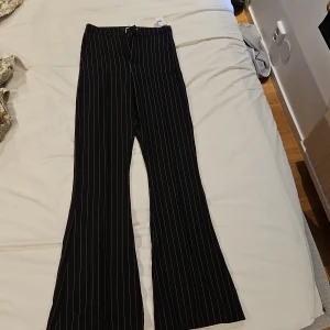 Svarta randiga kostymbyxor Gina Tricot - Snygga svarta kostymbyxor från Gina Tricot i storlek XXS. Byxorna har vita tunna ränder, vida ben och klassisk passform. Stängs med dragkedja, hake och knapp. Perfekta för en stilren look.