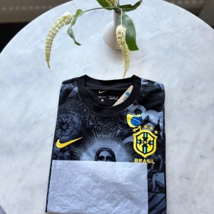 Nike Brasil svart fotbollströja M - Snygg svart Brasil-fotbollströja från Nike med unikt grafiskt tryck av Kristusstatyn och brasilianska symboler. Tröjan har korta ärmar, rund hals och är tillverkad i Dri-FIT-material som andas. Gula detaljer med Nike-logga och CBF-emblem på bröstet.