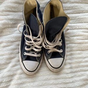 Helt oanvända Mörkblå Converse Chuck Taylor High - Klassiska mörkblå Converse Chuck Taylor All Star high-tops med vita snören och tåhätta som är helt oanvända bara prövade. Skorna har vit sula med svart rand och är tillverkade i canvas. Perfekta för en cool och avslappnad stil.