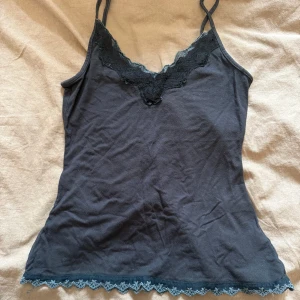 Svart linnetopp med spetsdetaljer - Svart linnetopp med tunna axelband och v-ringad halsringning dekorerad med svart spets😍. Nedtill finns en fin spetskant som ger en extra touch. Perfekt att styla lager på lager eller som den är. Har två stycken och säljer båda två!❤️Står ingen storlek men passar mig med S!❤️