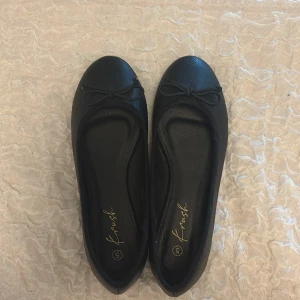 Svarta ballerinaskor - NYA ALDRIG ANVÄND! Stilrena svarta ballerinaskor från Bohoo med rund tå och söt rosettdetalj framtill. Skorna är gjorda i syntetmaterial med lätt textur och har platt sula för extra komfort. Perfekta att slänga på sig när du vill ha en enkel men snygg look. Säljer då dom tyvärr var för små för mig 