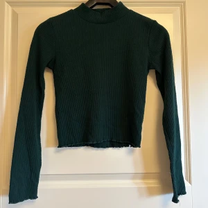 Mörkgrön ribbad långärmad stickad tröja Gina Tricot - Mörkgrön långärmad tröja med ribbad struktur och högre hals. Tröjan har en slim passform och är perfekt för lager-på-lager. Enkel och stilren design som funkar till många outfits.