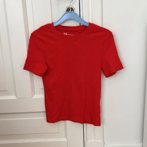 Röd ribbad topp med kort ärm - En enkel och snygg röd ribbad topp med rund hals och korta ärmar. Perfekt att matcha med jeans eller kjol för en clean look. T-shirten är i mjuk bomull och har en figurnära passform som känns både bekväm och trendig.