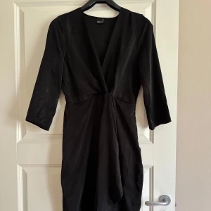 Svart fest nyår omlott klänning Gina Tricot - Snygg svart klänning från Gina Tricot med omlott-design och v-ringning. Klänningen har trekvartsärm och ett elegant fall framtill. Perfekt för dig som gillar stilrena och tidlösa plagg.