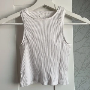 Vit ribbad ärmlös linnetopp - Säljer en fräsch vit ribbad linnetopp med rund halsriå.