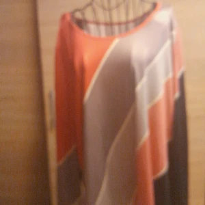 Randig långärmad blus 2XL - Säljer en långärmad blus i storlek 2XL med diagonala ränder i rött, svart, grått och beige. Blusen har en lös passform och är tillverkad i mjuk polyester med lite stretch. Perfekt för dig som gillar färg och mönster!