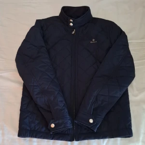 Mörkblå gant jacka - Snygg mörkblå quiltad jacka från Gant i storlek S. Jackan har hög krage med tryckknappar, dragkedja framtill och diskret logga på bröstet. Perfekt för kyliga dagar med sin klassiska look och bekväma passform. Den är som ny utan några som helst fel. Den säljs på grund av att den inte blir använd. Ny pris på jackan var 1.600