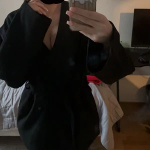 Svart Kappa - En jätte fin svart kappa från BikBok. Passar jätte bra till höst vädret men även sena lite kyligare sommarkvällar och till vintern med en stickad under. Den har inga skador, jag säljer pågrund av att jag köpt en ny fast i beige. Den går att knäppa men även bara användas med bandet, därför måste man inte ha den v/u ringad som jag har. Den har 2 styckna stora fickor som får plats med en del. Den passar alla storlekar från xxs-M. Pris kan diskuteras privat och ställ vilka frågor ni vill!❤️