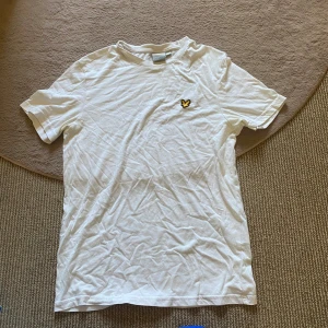 Lyle & Scott T-shirt  - Vit t-shirt från Lyle & Scott med klassisk passform och korta ärmar. På bröstet sitter den ikoniska gula örnloggan. Tillverkad i mjuk bomull som känns skön mot huden. Perfekt basic-plagg med stilren look!🙌🏻