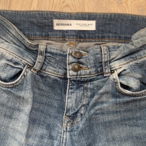 Blå bootcut jeans från Bershka - Säljer ett par blå bootcut jeans från Bershka med låg midja. Jeansen har snygg tvättad look, dubbla knappar i midjan och utsvängda ben. Perfekta för dig som gillar en retro vibe och vill ha ett par jeans som sticker ut lite extra. Är lite slitna längst ner!💗