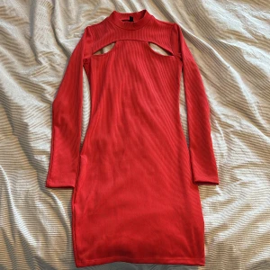 Röd ribbad långärmad klänning med cut out-detalj - Trendig röd ribbad klänning med lång ärm och hög hals. Snygg cut out-detalj framtill som ger en modern look. Klänningen är figurnära och passar perfekt för dig som vill sticka ut.