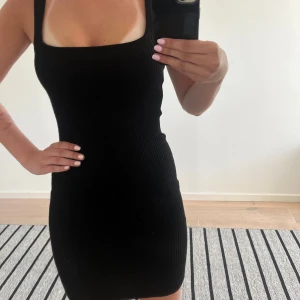 Svart enkel tajt klänning - Säljer en svart ribbad klänning från Stradivarius med fyrkantig ringning och breda axelband. Klänningen är tight och kort, perfekt för en trendig look. Materialet är stretchigt och bekvämt säljer då jag inte tycker den passar min stil längre! Andvänd max 2 gånger!