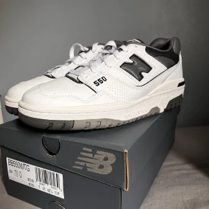 New Balance 550 - Säljer ett par helt nya New Balance 550 ” Castelrock” sneakers i vitt med svarta och grå detaljer. Perfekta för dig som gillar stilrena och sportiga sneakers. Passar även dig med storlek 41 EU. Skriv för mer information. Köp innan 25/07 för 600kr och levererar direkt!!!