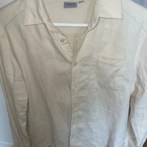 Beige linneskjorta  - Säljer en stilren beige skjorta från RYVLS i linne. Skjortan har klassisk krage, bröstficka och knäppning framtill. Perfekt för en avslappnad men ändå uppklädd look. Passar bra till både jeans och chinos och linnebyxor.