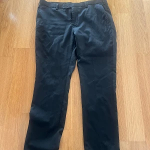 Svarta kostymbyxor från Dressmann - Klassiska svarta kostymbyxor från Dressmann med normal passform. Byxorna har raka ben och bälteshällor i midjan. Perfekta till skjorta eller kavaj för en stilren look.