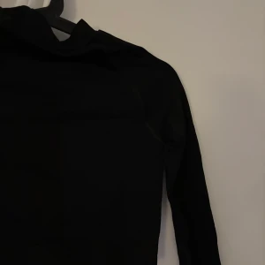 Svart långärmad träningströja från Boohoo FIT - Säljer en svart långärmad träningströja från Boohoo FIT. Tröjan har en tight passform och är tillverkad i ett stretchigt syntetmaterial som passar perfekt för träning. Enkel och stilren design utan synliga detaljer.