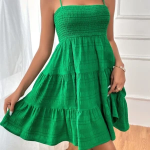 Grön sommarklänning med smock - Säljer en grön klänning med smock upptill och tunna axelband. Klänningen har en luftig och voluminös kjol med volangdetaljer och är perfekt för varma dagar. Den är ärmlös och har en kort längd som ger en fräsch och ungdomlig look. OANDVÄND