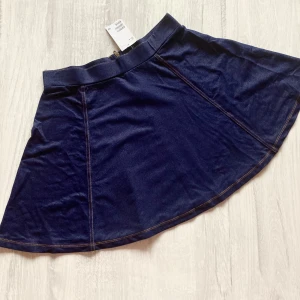 Mörkblå jeanskjol med utsvängd form - Säljer en mörkblå jeanskjol med utsvängd passform och synliga kontrastsömmar. Kjolen har bred linning och är i en kort modell, perfekt att styla med sneakers eller boots.