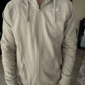 Beige hoodie med dragkedja från Gymshark - Säljer en beige hoodie från Gymshark med dragkedja framtill och två fickor. Skön tröja och bra kvalité, passar till de mesta !