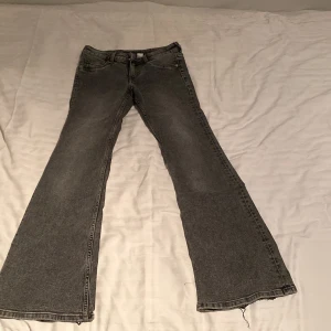 Grå bootcut jeans från Divided H&M - Säljer ett par grå bootcut jeans från Divided H&M i storlek 38. Jeansen har utsvängda ben och råa, fransiga benslut för en cool look. Klassisk femficksmodell och normal passform i midjan. Dem är slitna nere vid byxorna men märks knappast!