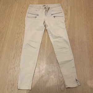 Beige jeansbyxor från Zara Basic Dept. - Snygga beige jeansbyxor från Zara Basic Dept. med smal passform och dragkedjedetaljer framtill. Byxorna har hög midja och klassiska bakfickor. Perfekta för en stilren och modern look.