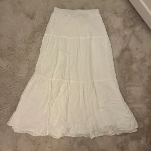 Vit långkjol med volang - Säljer en vit långkjol med volangdetaljer. Kjolen har en luftig och flowy känsla, perfekt för varmare dagar. Enkel och stilren design som är lätt att matcha med olika toppar.