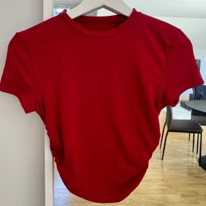 Röd t-shirt med rynkade sidor - Säljer en röd t-shirt med en snygg rynkdetalj på sidorna som ger en fin form. Perfekt till jeans eller kjol.