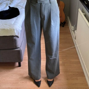 Grå kostymbyxor med hög midja - Snygga grå kostymbyxor med hög midja och raka, vida ben från djerf avenue. Byxorna har pressveck framtill och diskreta fickor bak. Använt men fint skick. 200kr + frakt